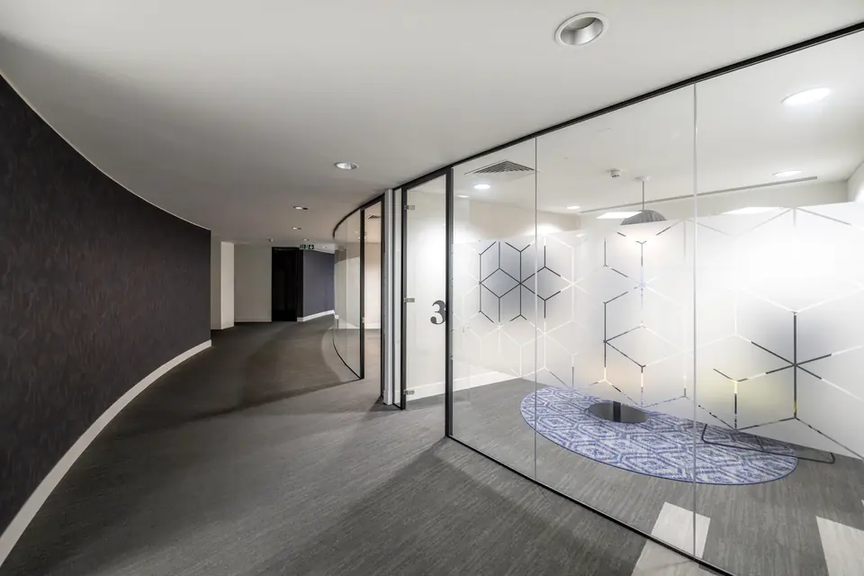 Curved glass meeting room along a sweeping office corridor
